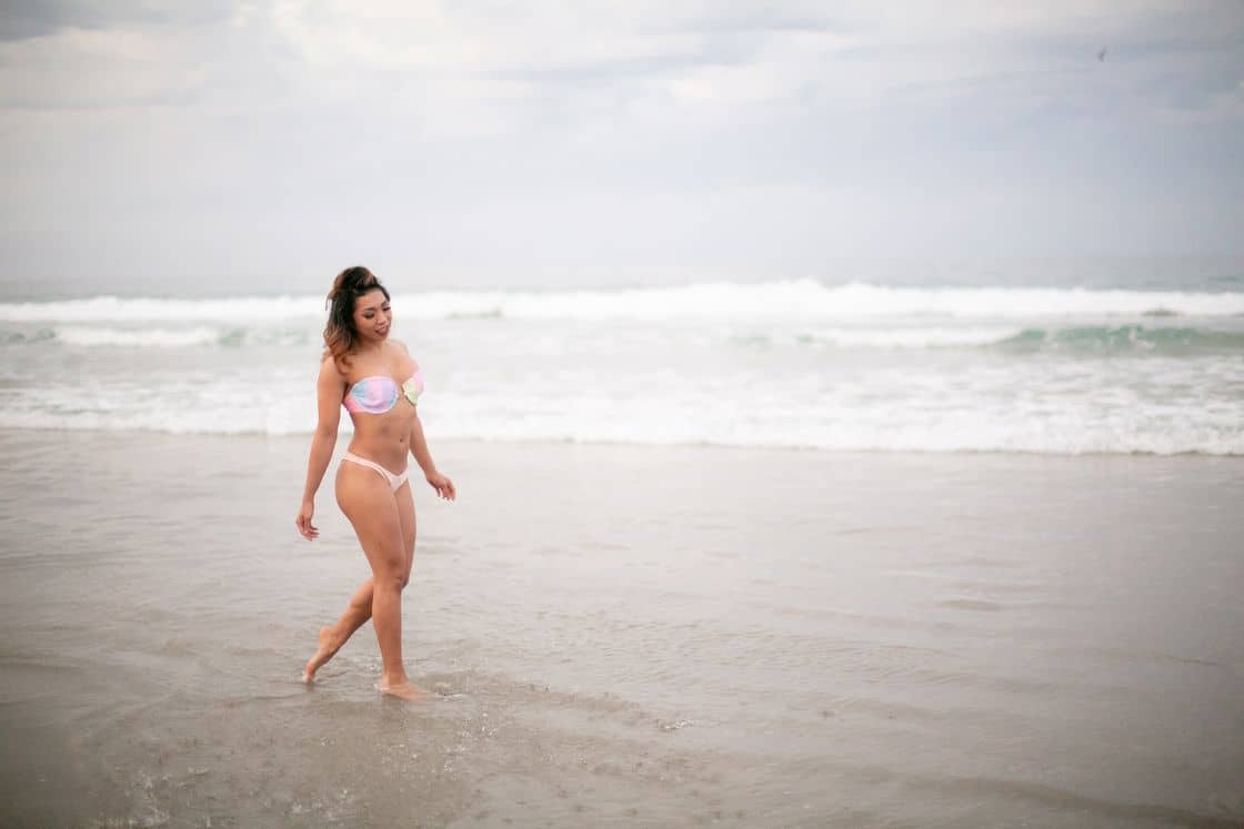 Woman wearing a two piece pastel colored bikini set while walking on the edge of a beach
