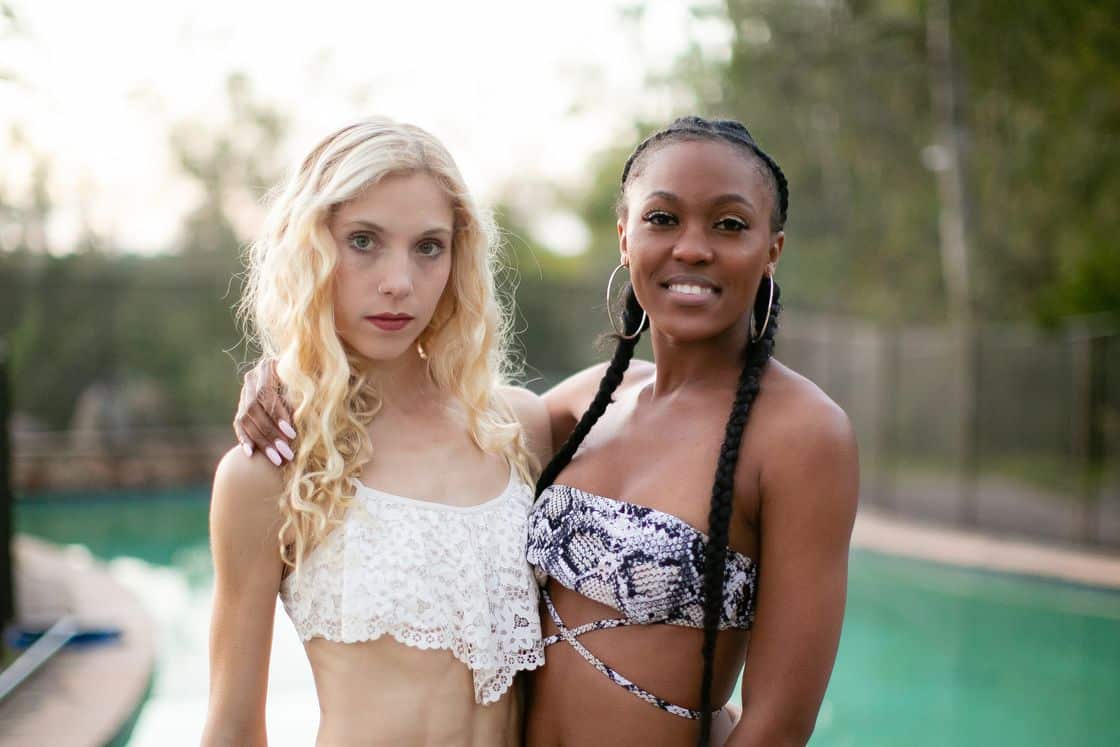 Woman with a white lacy bikini top posing with a woman wearing a snakeskin bikini top near the edge of the pool