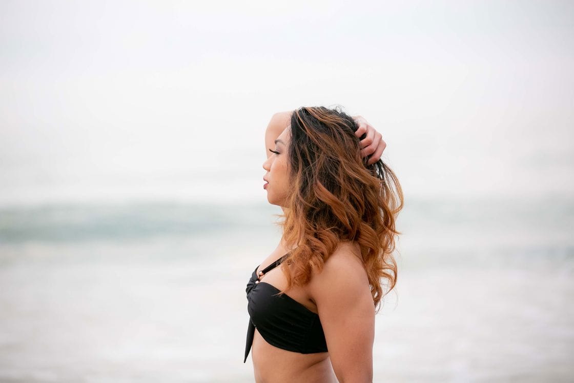 Woman wearing a black bikini top posing sideways near the beach