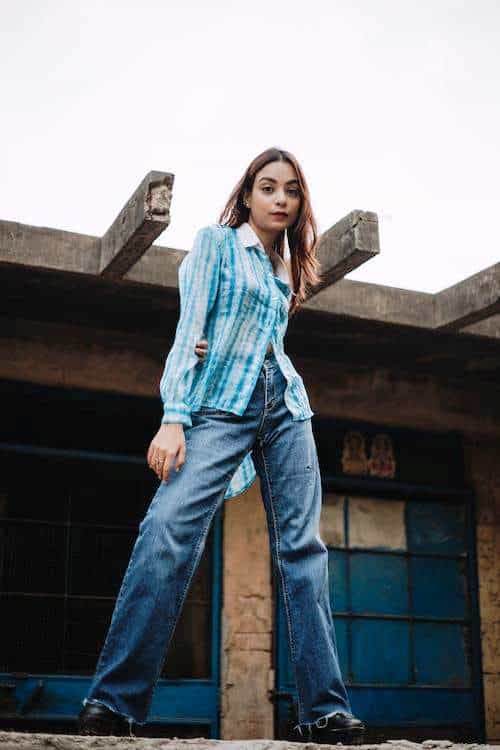 Woman wearing a blue long sleeved top and blue jeans posing outside an old house for a shoot