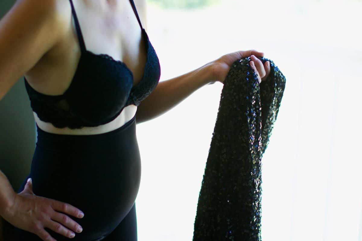 A woman wearing a black bra and fitted bottoms while holding a bodycon dress
