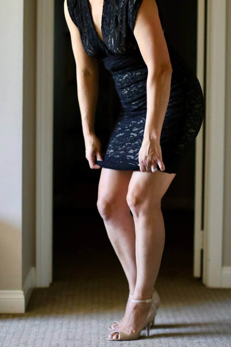 A woman wearing a black bodycon dress pulling it downwards to fit