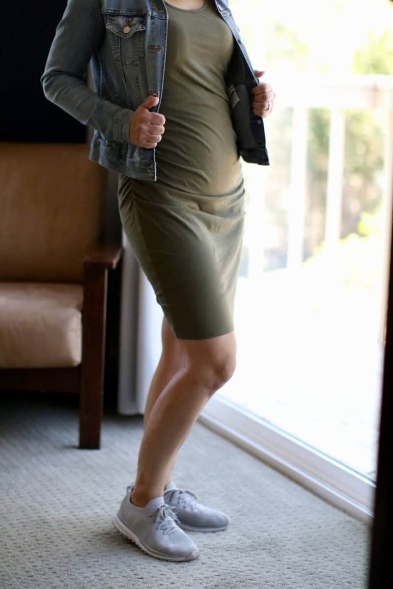 A woman wearing a bodycon dress partnered with a denim jacket and grey sneakers