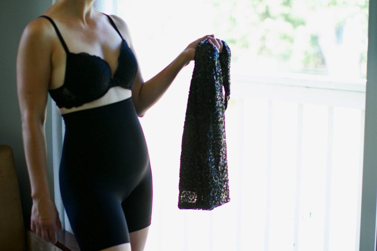 A woman wearing a fitted innerwear for bottoms and a bra while holding a bodycon dress