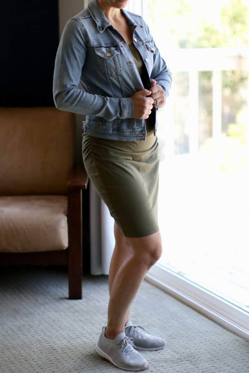 A woman wearing a bodycon dress with a denim jacket and sneakers