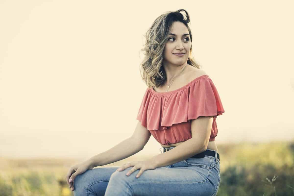 A woman sitting wearing an off-shoulder tops and jeans with belt
