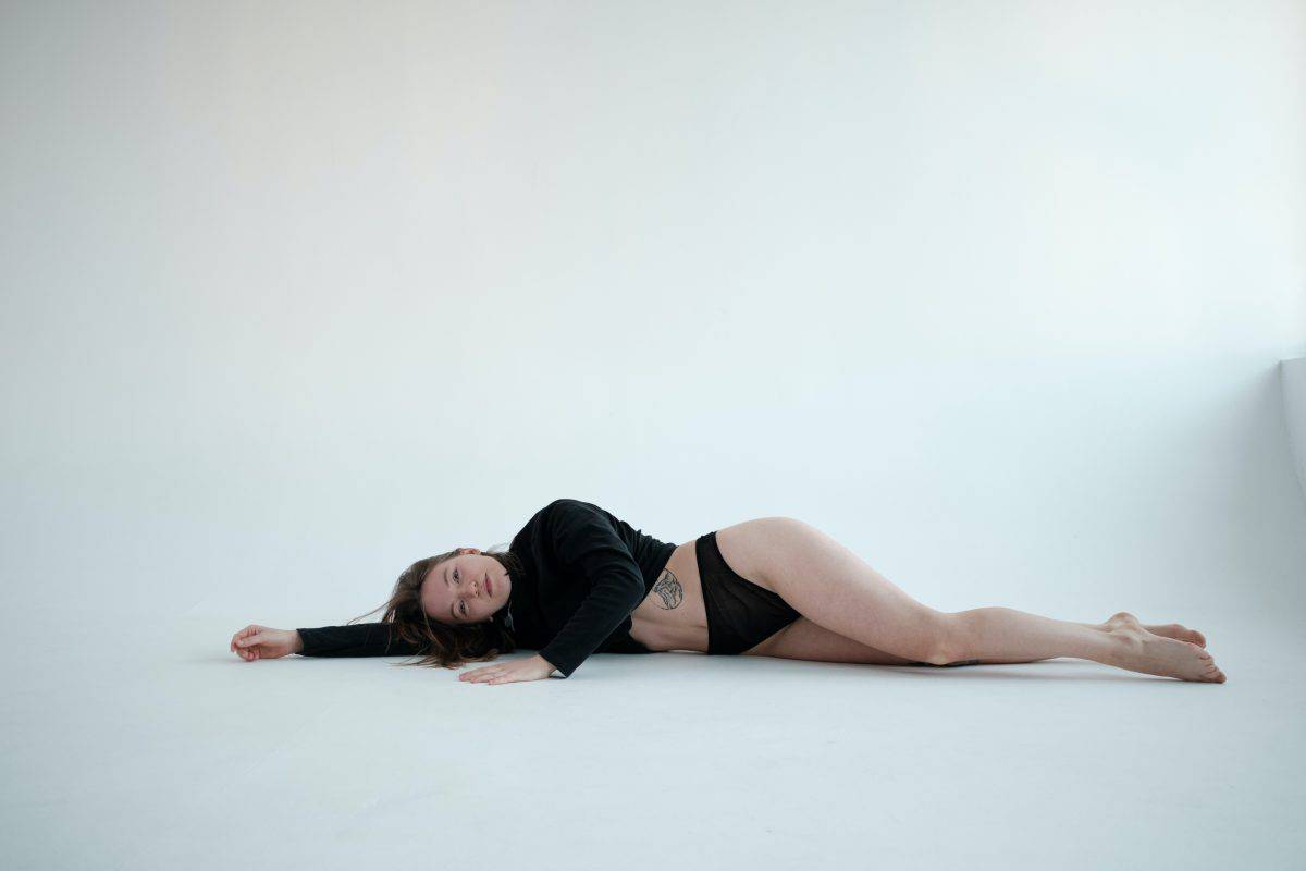 A woman wearing black long sleeves and high wasted underwear laying down on a white ground