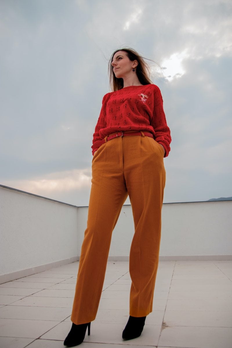 A woman wearing a red sweater and mustard chino pants with black shoe high heels