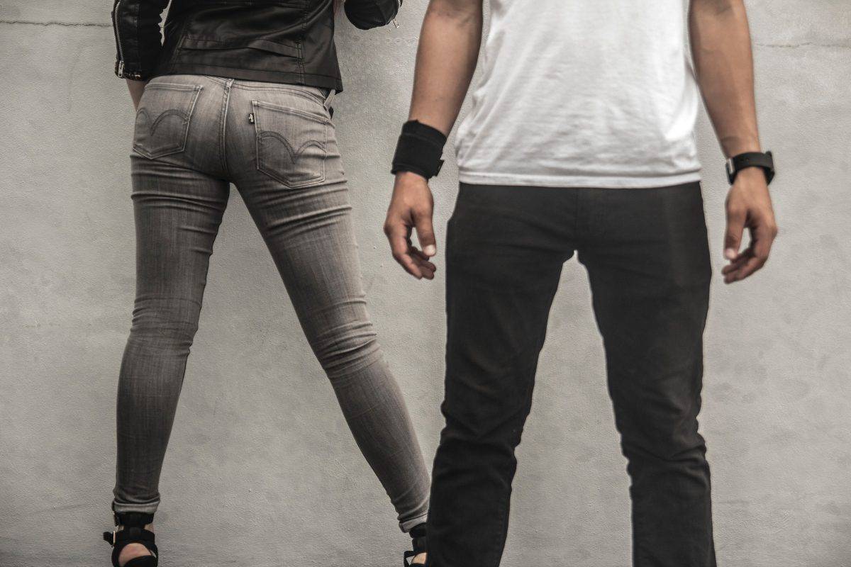 A man and woman facing on opposite sides wearing gray and black fitted jeans